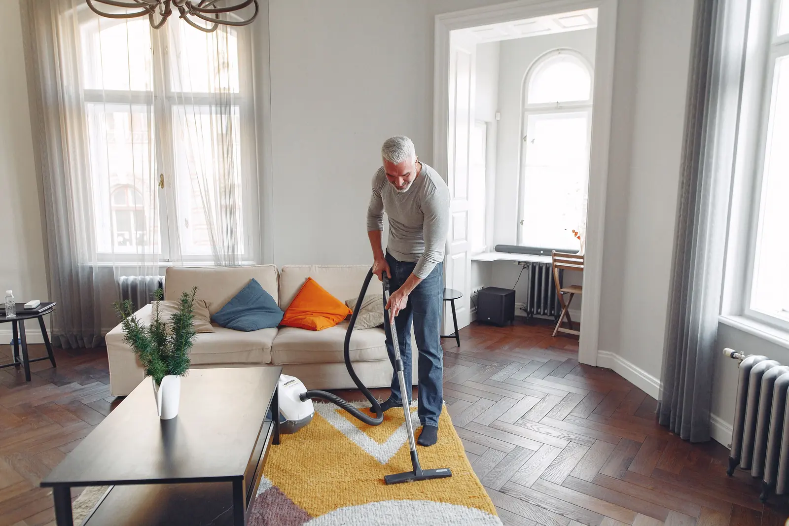 Person working a cleaning head across carpet in a bright living room with tall windows