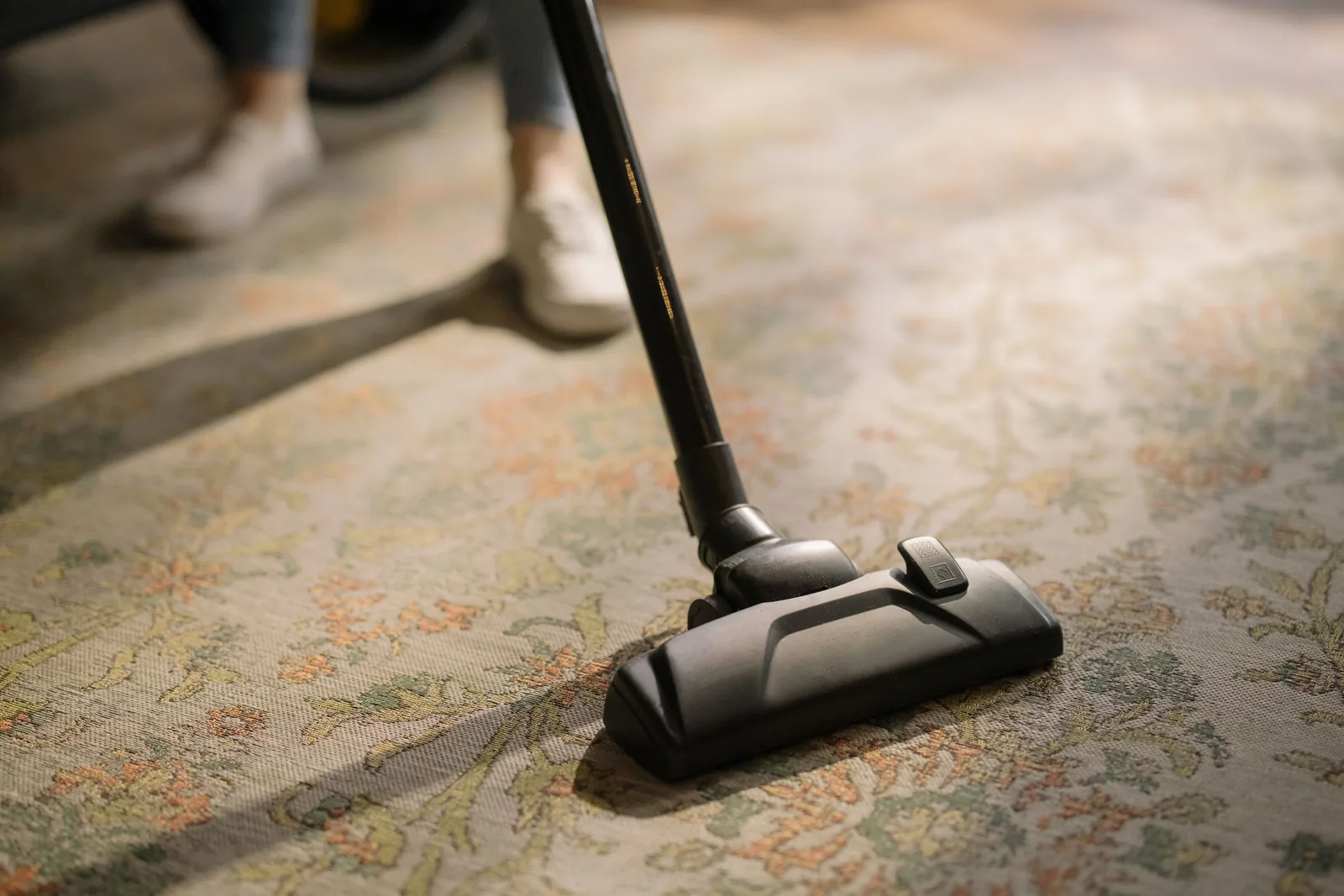 Close-up of a cleaning head being worked across a patterned carpet in a sunlit room